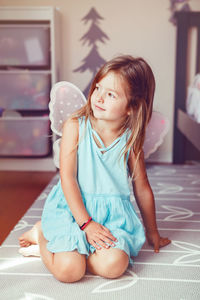 Cute girl sitting dressed up in fairy looking away at home