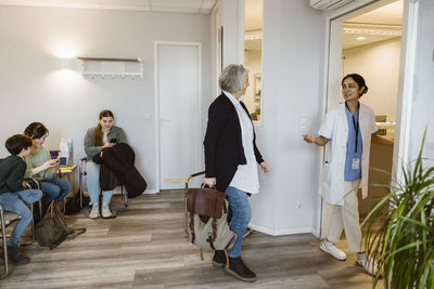 Senior female patient walking towards medical examination room with doctor in clinic