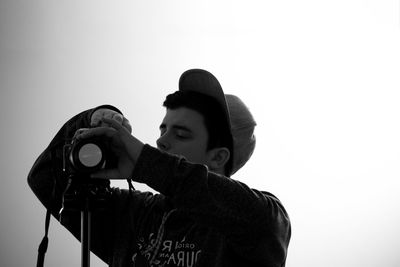 Young man adjusting camera against clear sky