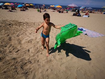 Full length of shirtless boy holding inflatable raft on beach