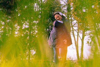 Young woman standing by tree in forest