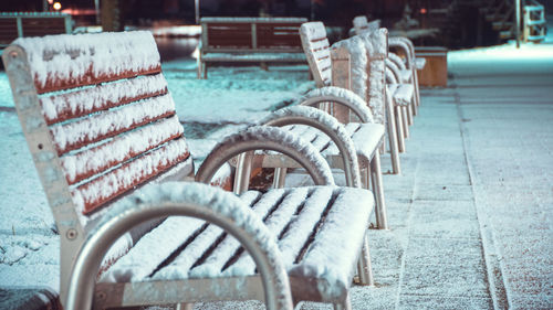 Snow covered chairs by footpath at night