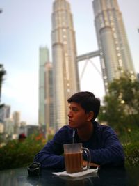 Young man with coffee in city against twin towers