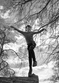 Low angle view of boy standing by bare tree