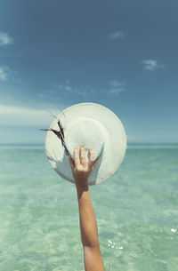 Person holding umbrella by sea against sky