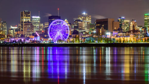 Illuminated ferris wheel in city against sky at night