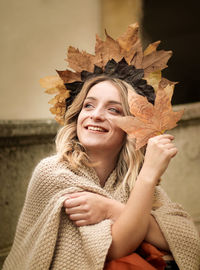 Smiling young woman holding autumn leaves looking away outdoors