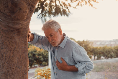 Young man standing against tree trunk