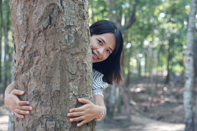 Portrait of young woman against tree trunk in forest