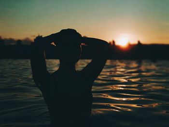 Silhouette woman standing by lake against sky during sunset