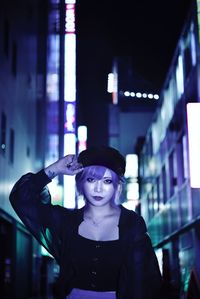 Portrait of young woman wearing hat standing at night