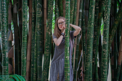 Portrait of young woman standing against bamboo plants