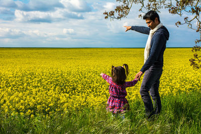 Father and daughter holding hands while standing on field against sky