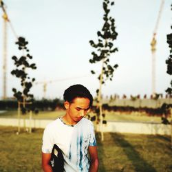Portrait of young man standing on field against sky