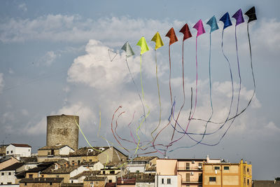 Low angle view of kites over buildings against cloudy sky on sunny day