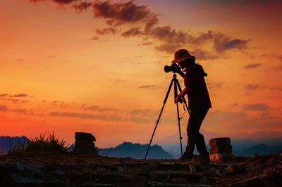 Silhouette man photographing against orange sky