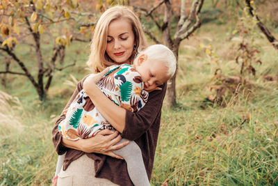 Mother carrying daughter while standing on grassy land