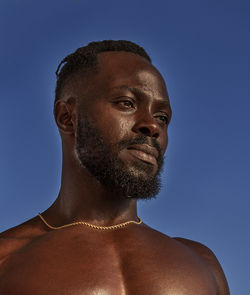 Portrait of shirtless man against blue sky