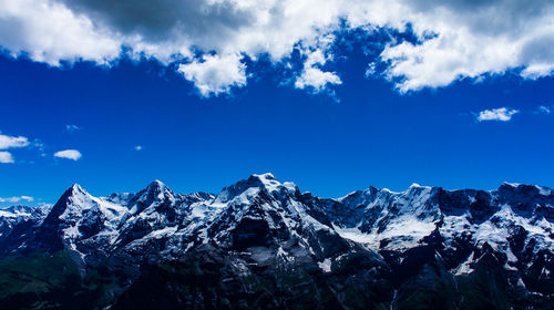 Low angle view of snowcapped mountains against blue sky