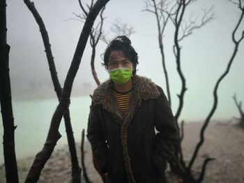 Portrait of man wearing surgical mask while standing against trees during winter