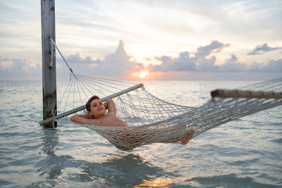 Low section of woman swimming in sea against sky during sunset