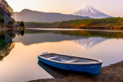 Boat moored at lakeshore against mt fuji during sunset