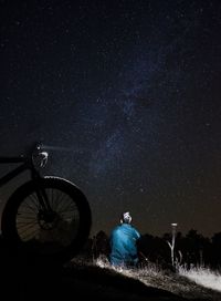 Rear view of man sitting on field against sky at night