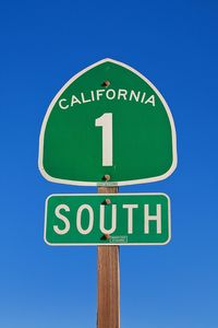 Low angle view of road sign against clear blue sky