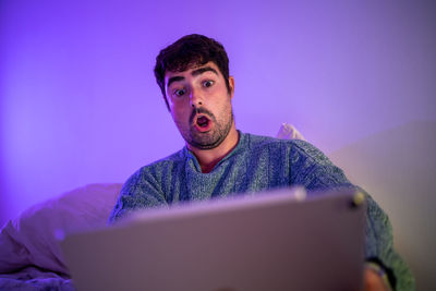 Man using digital tablet sitting on bed against wall at home