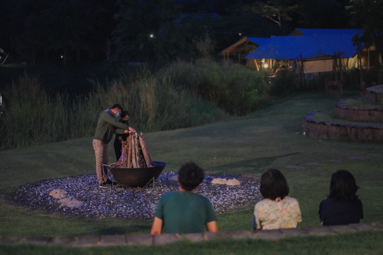 REAR VIEW OF PEOPLE SITTING AT ILLUMINATED PARK