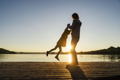 Mother spinning daughter over pier during sunset