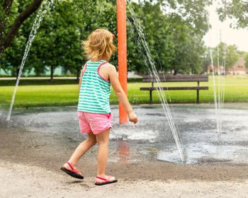 Little smiling child playing with water at splash pad in the local public park on hot summer  day