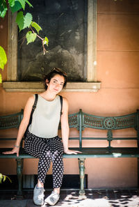 Portrait of smiling young woman sitting against wall