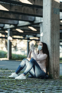 Full length of woman wearing mask sitting outdoors