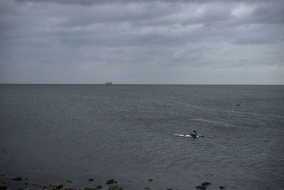 Boats sailing in calm sea against cloudy sky