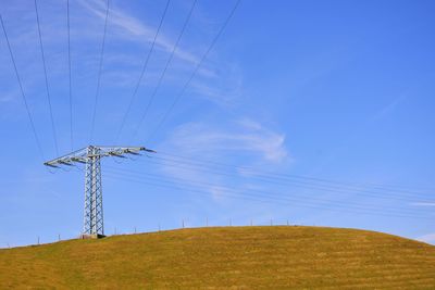 Low angle view of electricity pylon on field against blue sky