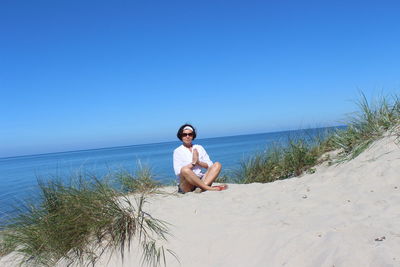 Young woman sitting on beach against clear sky