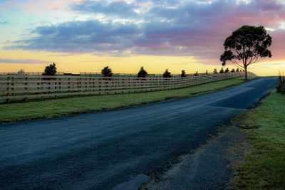 Empty road amidst field against sky during sunset