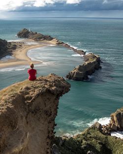 Rear view of woman sitting on cliff by sea