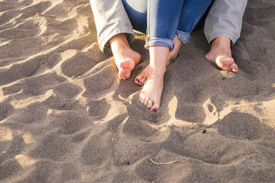 Low section of friends sitting on sand at beach