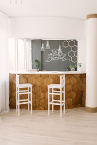 A stylish modern bar counter decorated with wooden tiles and two white bar stools in the living room