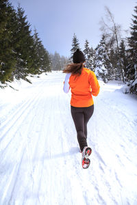 Rear view of woman running on snow covered field against sky