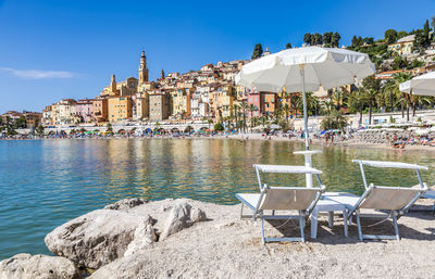 Chairs by swimming pool at beach against blue sky