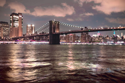 Illuminated bridge over river against sky at night