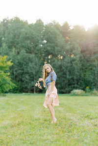 Young pretty woman in a summer dress walks through a meadow on green grass. a young girl holds shoes