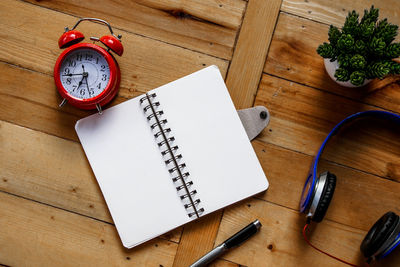 Directly above shot of alarm clock with spiral notebook and potted plant on wooden table
