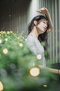 Young woman looking down while standing against illuminated lamp