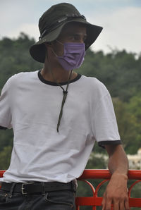 A young man standing outside with wearing face mask and hat during coronavirus pandemic 