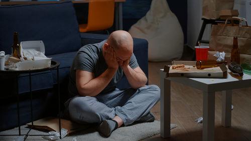 Tired man sitting cross-legged on floor at home