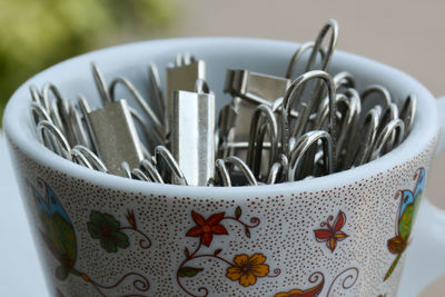 Portrait of a tiny cup filled with metal binder clips on a white surface 